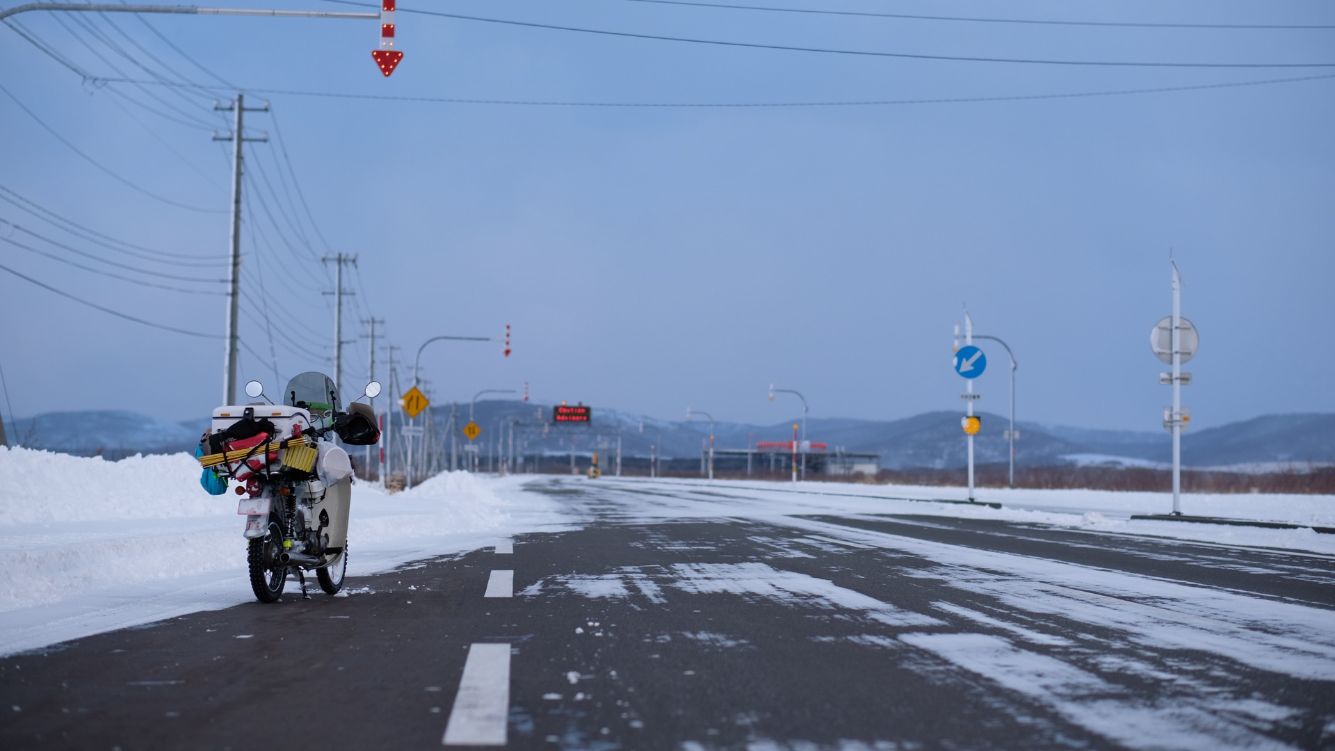 雪道に佇む荷物満載のバイクと夕暮れの空
