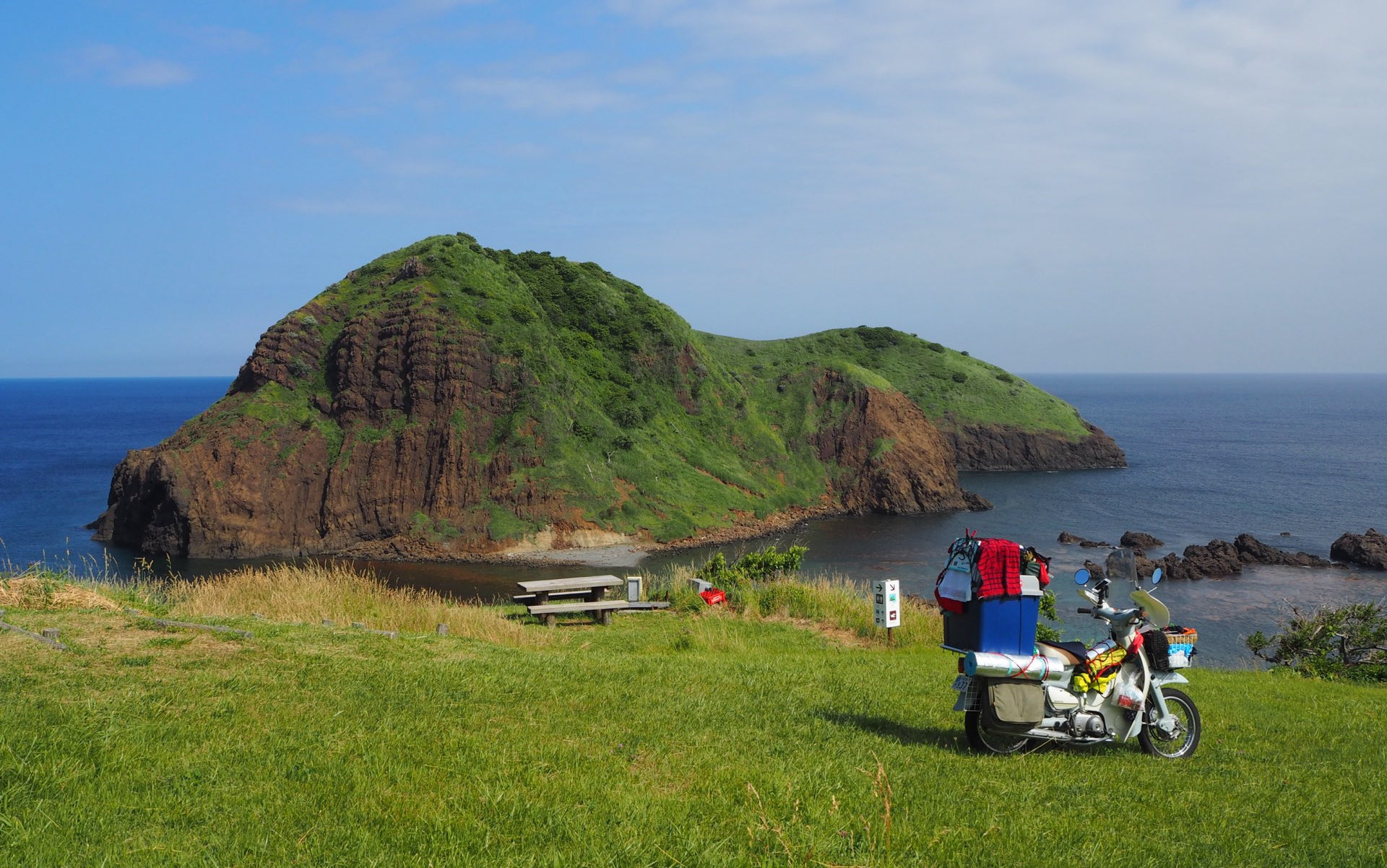 緑の岩山と海を望むキャンプ地のバイク